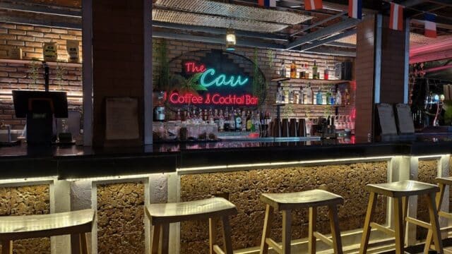 A cozy Hoi An bar with stools, a neon sign for The Cau Coffee & Cocktail Bar, and bottles lining the shelves.