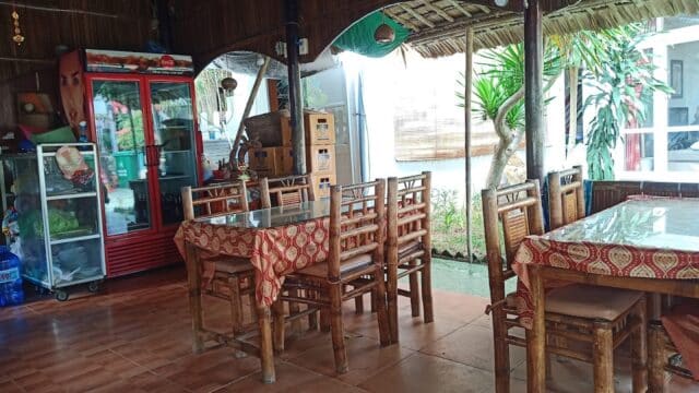 Bamboo chairs and tables with patterned cloths fill this rustic, open-air Hoi An restaurant featuring a red fridge and glass display case.