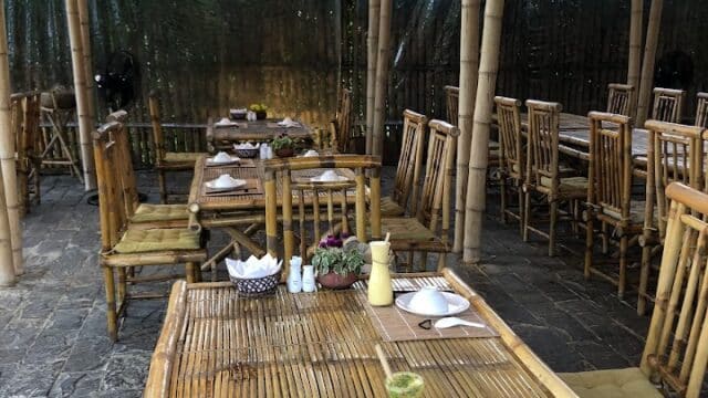 Bamboo tables and chairs set for a meal in an open-air Hoi An restaurant with warm hanging lights.