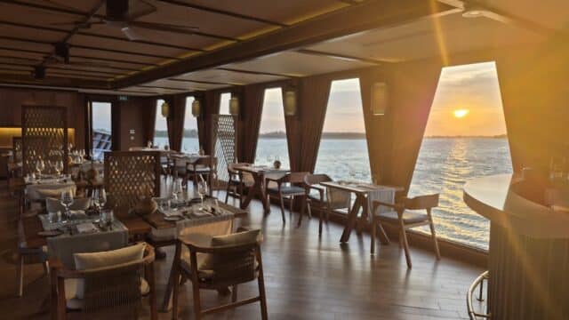 Elegant Hoi An restaurant with wooden decor, set tables, and large windows overlooking a sunset on the water.