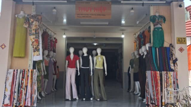 A clothing shop in Hoi An with mannequins in stylish outfits, fabric rolls on both sides, and a sign above the door.
