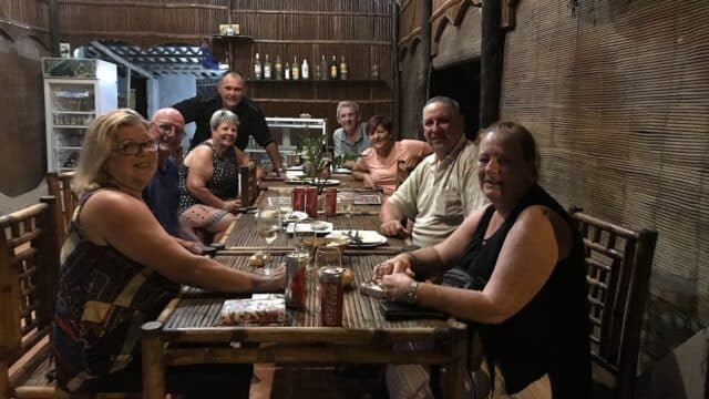 Eight adults sit around a wooden table in a cozy, dimly lit Hoi An restaurant, smiling warmly at the camera.