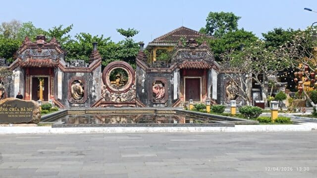 Ancient temple entrance with ornate carvings in Hoi An, reflected in a pool and surrounded by greenery under a clear sky.