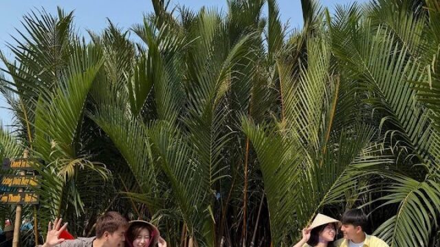 Two couples sit in colorful round boats on a river in Hoi An, surrounded by lush green palms beneath a clear blue sky.