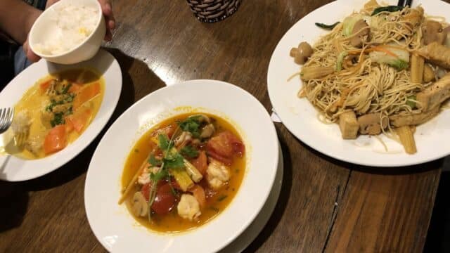 Plates of Thai food with noodles, curry, soup, and a bowl of rice on a wooden table in Hoi An.