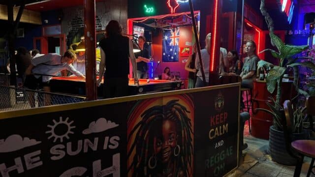 People play pool at a lively, neon-lit Hoi An bar with reggae-themed art and an Australian flag on the wall.