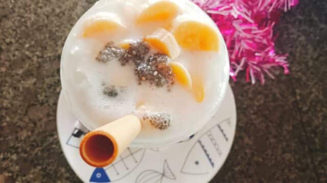 A glass of fruit and chia seed dessert with a wafer stick sits on a fish-patterned plate, evoking vibrant Hoi An charm.