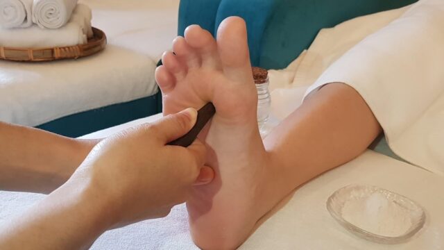 A person receives a soothing foot massage with a wooden tool in a tranquil Hoi An spa setting.