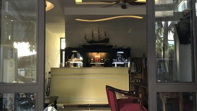A cozy Hoi An café with a yellow counter, red chairs, and a ship model on a shelf, seen through open glass doors.