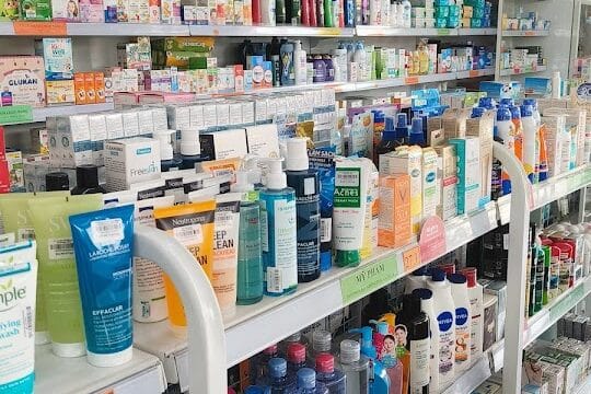 Shelves in a Hoi An pharmacy display skincare products, medicines, and health items beneath rows of red flags with yellow stars.