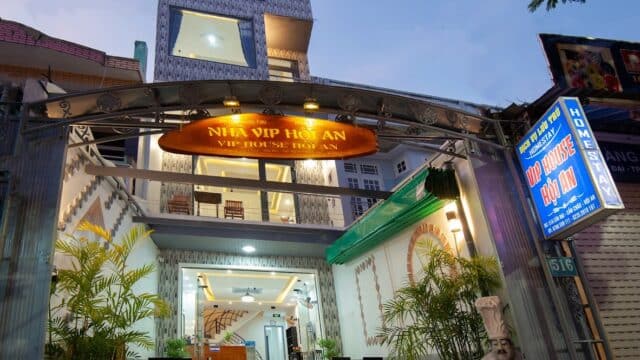 Entrance of a Hoi An guesthouse with a lit NHÀ VIP HOÀN sign, outdoor seating, and potted plants, captured at dusk.