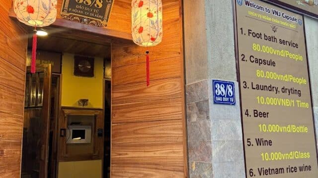 Wooden entrance with hanging lanterns, a signboard listing services and prices, and address number 38/8 in Hoi An.