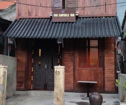 A two-story wooden building with lanterns in Hoi An, labeled VNJ Capsule 159, and a small table outside.