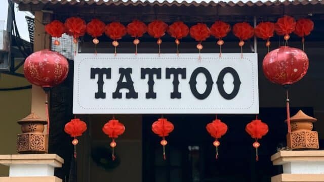 A storefront in Hoi An with a TATTOO sign, decorated with red lanterns and hanging red ornaments.