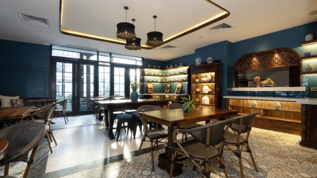 A cozy, modern café in Hoi An with wooden tables, blue walls, decorative shelves, and large windows letting in natural light.