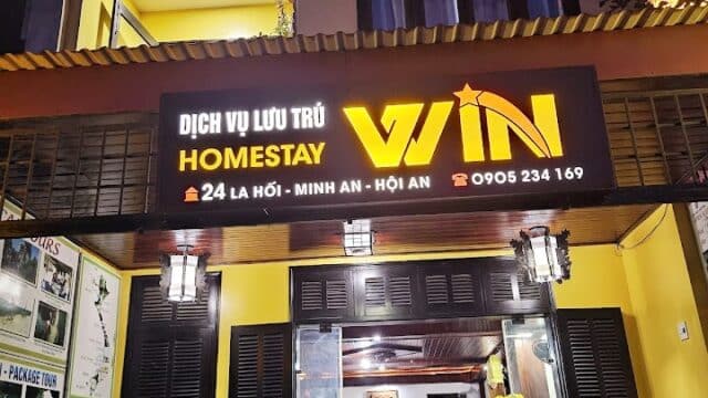A yellow homestay building at night in Hoi An with a bright WIN HOMESTAY sign above the entrance.