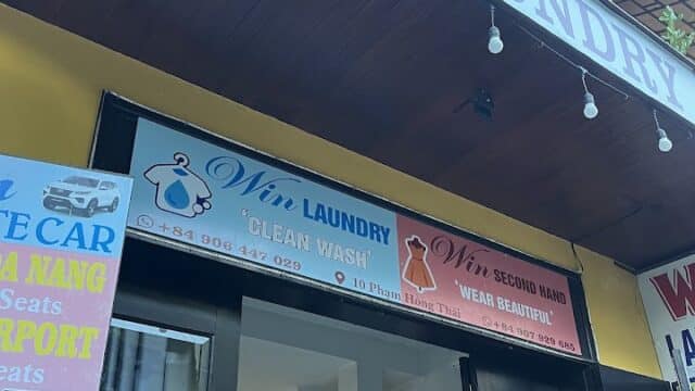 Shopfront of Win Laundry in Hoi An with signs for laundry, secondhand clothing, and garments visible through glass doors.