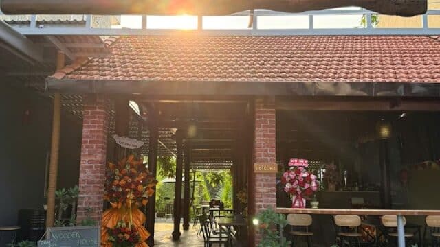 Wooden House café-restaurant-bar entrance in Hoi An, with flowers, stools, tables, and an OPEN signboard under a sunny sky.