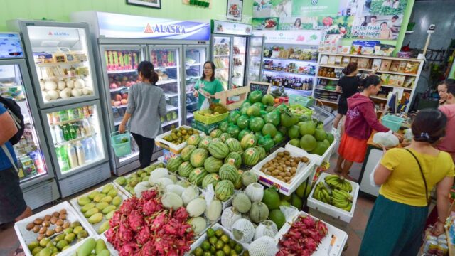 People shopping in a small Hoi An grocery store filled with fresh fruits, vegetables, and refrigerated drinks.