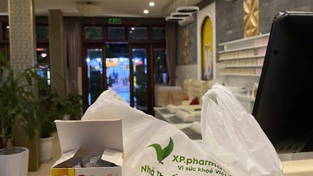 A pharmacy counter in Hoi An features a white bag and GASVIC medicine, with shelves and plants in the background.