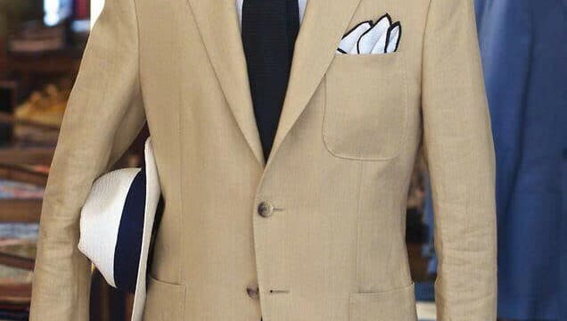 Tan suit on a mannequin with a white shirt, black tie, folded pocket squares, and a white hat in the left hand—perfect for Hoi An style.
