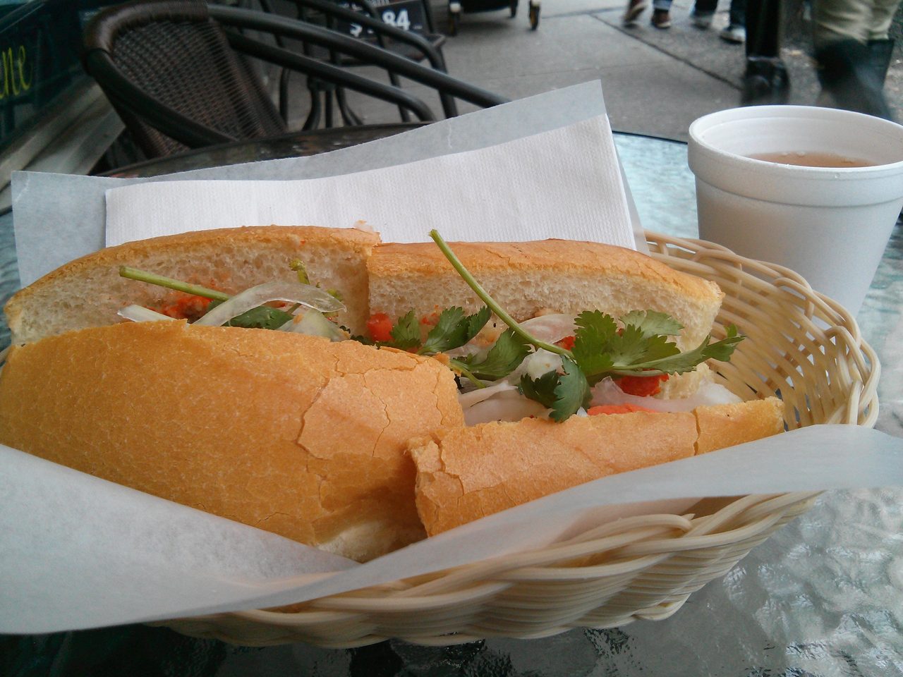 A Vietnamese banh mi sandwich with pate, pickled carrot and cilantro in a takeaway basket