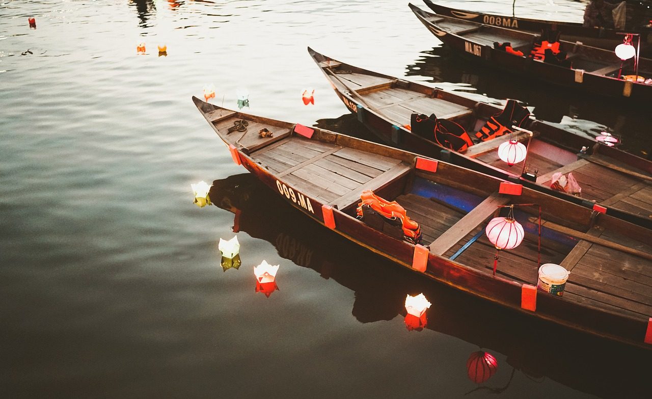 Wooden boats decorated with lit paper lanterns floating on the Thu Bon river in Hoi An at night